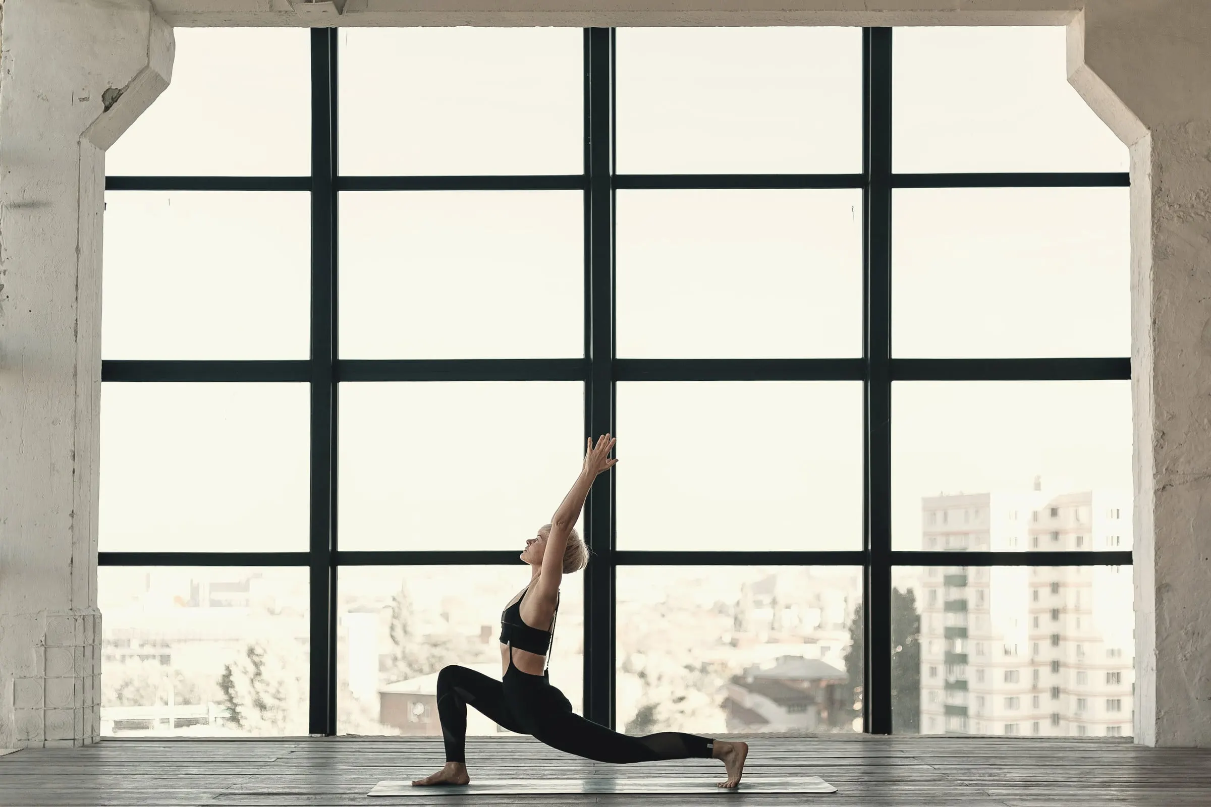 Donna in una posizione di yoga davanti a una grande vetrata luminosa